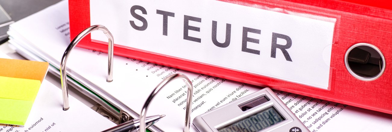 Kugelschreiber, Taschenrechner und ein Aktenordner mit der Aufschrift Steuer © iStock/gopixa